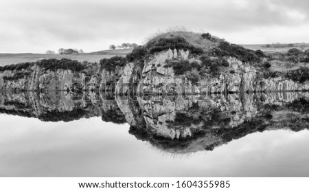 A section through the Whin Sill reflected in a lake in Northumberland, England.  Royalty-Free Stock Photo #1604355985