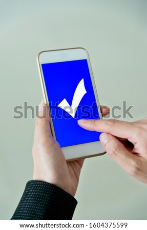 Closeup of hand holding smartphone with vote button on the screen.