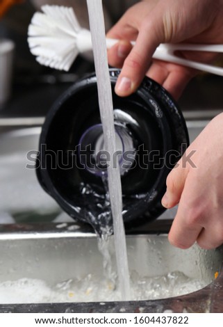 Doing dishes after cooking at home. Caucasian male doing the dishes. Closeup image. In this photo there is a top of smoothie blender being washed with some soup bubbles and running water. Color photo.