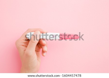 Young woman hand holding pregnancy test with two stripes. Pastel pink color background. Positive result. Closeup. Point of view shot.  Royalty-Free Stock Photo #1604457478