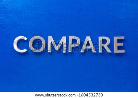 the word compare laid with silver metal characters on blue painted wooden board in flat lay with central composition