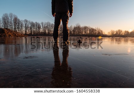 Young man standing on ice in pond with sun and trees, close up photo.