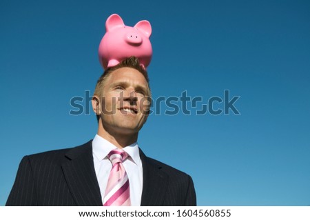 Businessman balancing a pink piggy bank on his head outdoors in bright blue sky