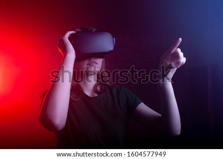 young girl in virtual reality glasses at night in the game room, a woman surprised in virtual space