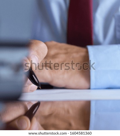 Man signing a document or writing correspondence with a close up view of his hand with the pen and sheet of notepaper on a desk top.