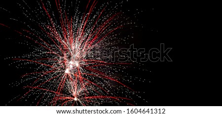 Colorful sparkly red and white fireworks in the sky against black background 