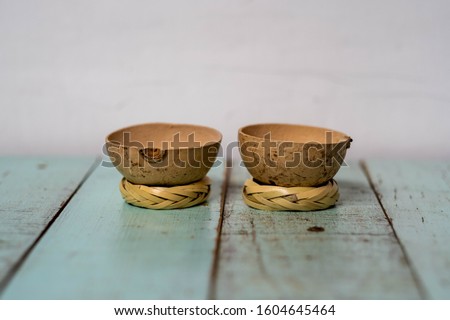 Two traditional "jicama" cups for drinking mezcal in Mexico, on their "rodete" stands. Cups made from the skin of the gourd fruit of a jicama tree. On a rustic vintage wood table painted green. Royalty-Free Stock Photo #1604645464