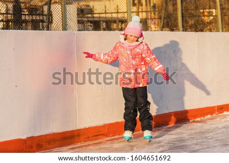 A little Girl learns to skate, she holds on to the side of the hockey court