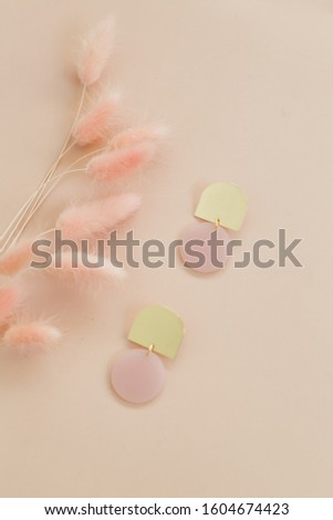 Pink and gold earrings on pink background with dried pink grass