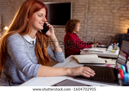 Business people working in a modern office, woman having a phone conversation while man working on a laptop computer; freelancers working in coworking space