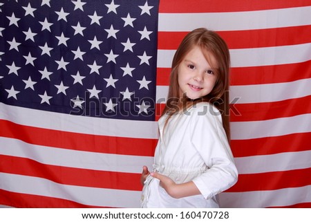 Caucasian young beautiful girl in a white jacket is standing on a of the American flag