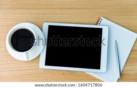 Digital tablet with coffee, paper and pen on wooden table.