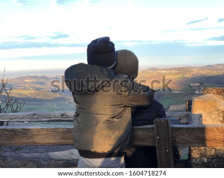 Son hugs father sitting on bench across mountains view and setting sun. Family time. family tourism