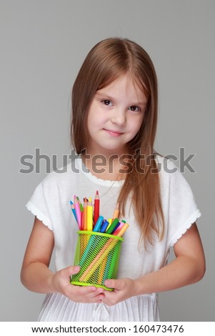 Happy little girl drawing with pencils on gray background on Education