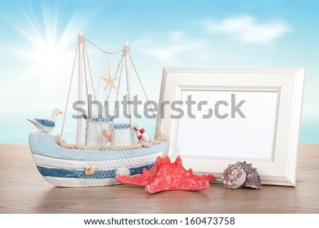 Photo frame, starfish, seashell and decor boat on wood table over sunny sea background