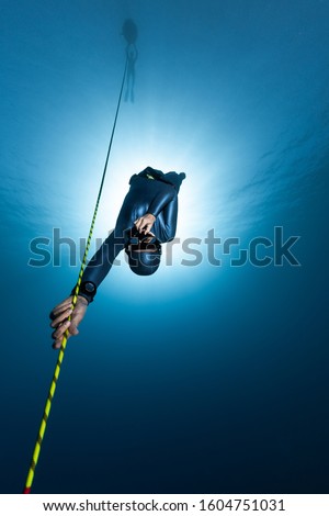 Freediver descends along the rope into the depth while another freediver relaxes on the buoy Royalty-Free Stock Photo #1604751031