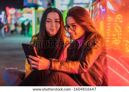 Young girls looking at the smartphone and smiling near neon lights at night