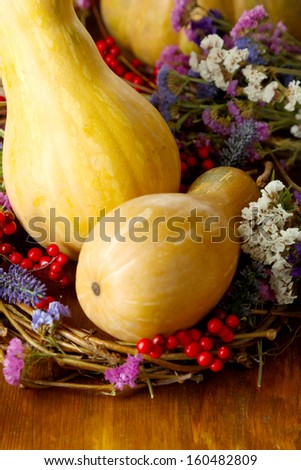 Pumpkin in wreath of dry branches with flowers and viburnum on wooden table close-up