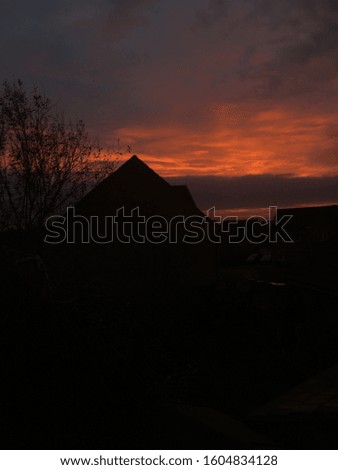A beautiful cloudy sunset, orange. With clouds blocking the sun shine brightly, and houses in the foreground bringing depth into the picture.