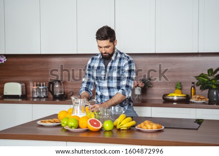 Attractive gentleman sitting at kitchen table and cutting orange stock photo