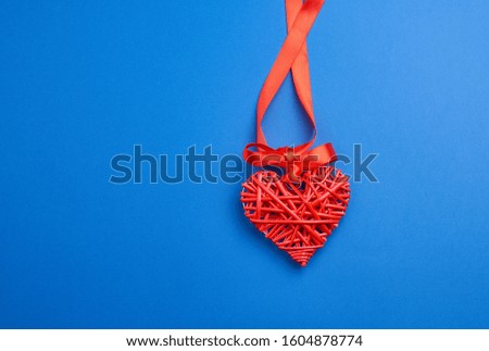 red wicker decorative heart hanging on silk ribbon, blue festive background for Valentine's day, copy space
