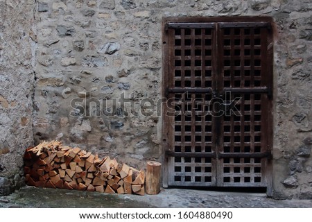Neatly Stacked Pile of Chopped Fire Wood Logs for Winter Beside Old Metal Portcullis Gate Door with Stone Wall background in a Medieval Castle Chateau in Switzerland