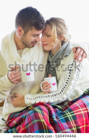 Loving young couple in winter clothing with coffee cups against bright background
