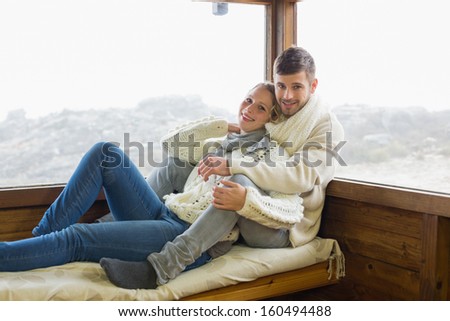 Portrait of a young couple in winter clothing sitting against cabin window