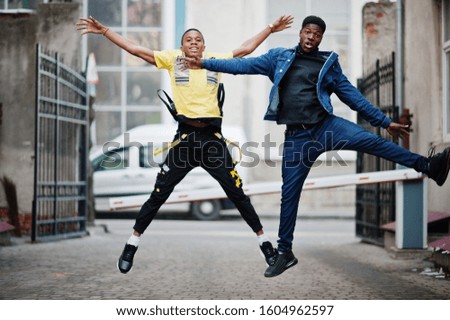 Two african male friends jump together.
