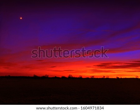 Picture of evening sunset with vivid colours and silhouetted foreground. Moon in to left corner. 