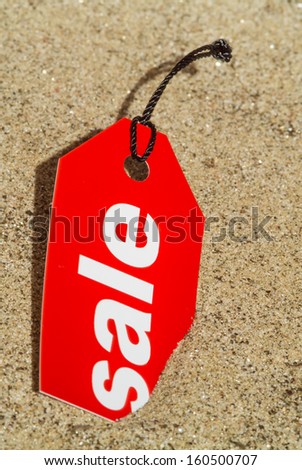 Macro photo of a red sale tag on a sandy beach