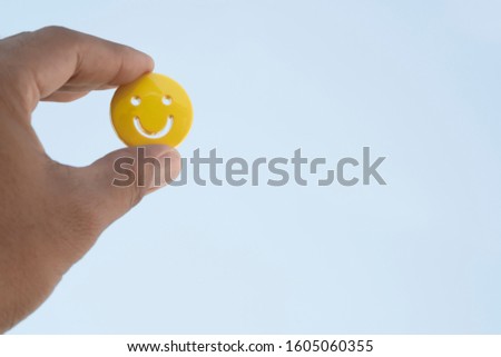 Male hand holding yellow emoticon smiley face icon symbol on blue sky background with copy space, for a positive mindset in business marketing and beautiful world peace concept