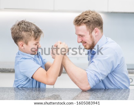 Happy father and son competing in arm wrestling at home