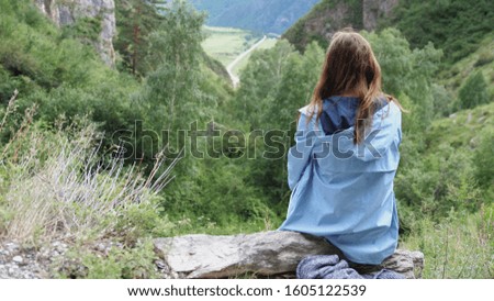 A young woman sits on a background of mountains with flying hair