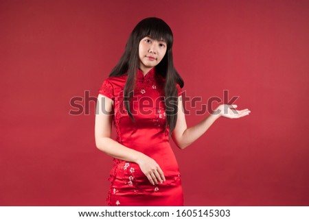 Elegant Asian woman wearing cheongsam and smiling to you to show something. Chinese new year picture.