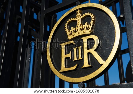 Queen Elizabeth Regina sovereign's cypher symbol with crown in gold on black iron gate, a monogram displayed on government buildings, documents, mail boxes, money and official apparatus