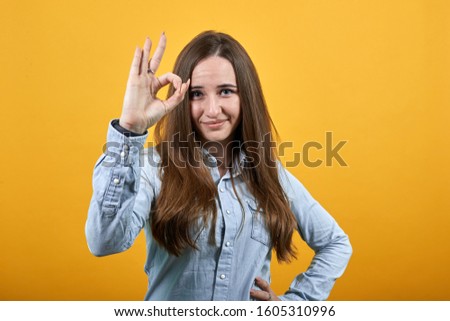 Cheerful charming caucasian woman wearing fashion shirt isolated on orange background in studio doing okay gesture, smiling. People emotions, lifestyle concept.