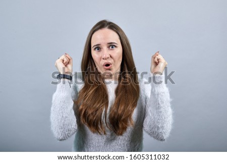 Cheerful charming caucasian woman wearing fashion blue sweater, dancing, smiling, keeping fist up isolated on gray background in studio. People emotions, lifestyle concept.