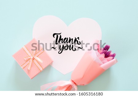 Bouquet of stabilized flowers, gift box and paper heart on blue background. Thank you lettering on paper heart