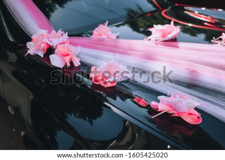 Wedding decorations closeup in the form of paper flowers on the hood of a black car. Wedding details, picture, concept.