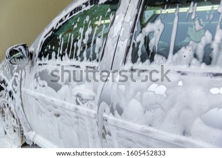 a car covered by soap foam while washing indoors - close-up with selective focus