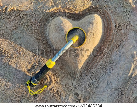 The photo of an underwater metal detector and a  sand heart on the beach.Treasure searching and tourist adventure background.