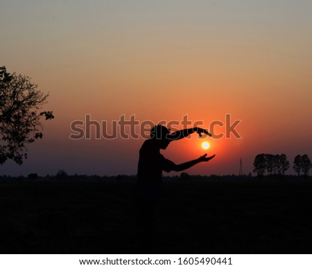 Silhouette of young man praying over sunset background.