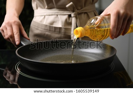 Woman pouring cooking oil from bottle into frying pan, closeup Royalty-Free Stock Photo #1605539149