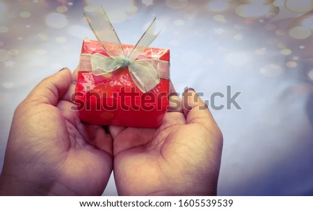 A red gift box on hands with copy space bogey background close up view, love concept, romantic idea, friendship concept, happy new year idea, image