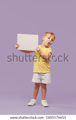 Little child boy holding a white banner on purple background. Funny Face. Copy space for text