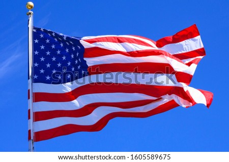 Majestic flag of the United States of America flying in the wind. Clear blue sky in background. 