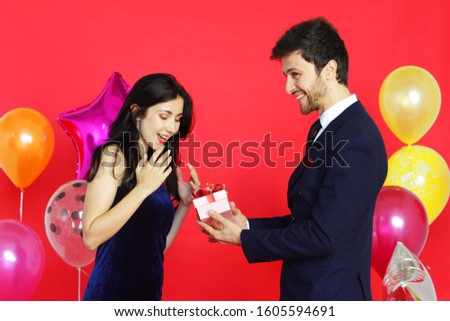 Sweet couple Love happy with surprise gift box girlfriend in christmas party, Birthday time celebration new year eve, Valentine day decoration with colorful balloon on red background