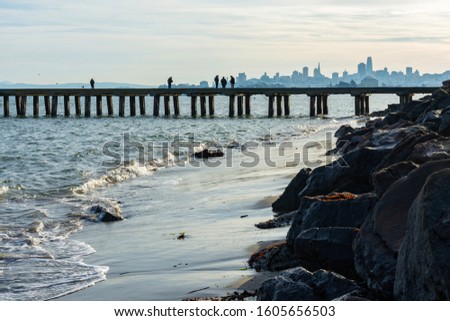 Morning on San Francisco Bay. Fishermen on a pier,  surf, san and stones under grey sky