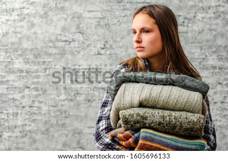 portrait of young teenager brunette girl with long hair holding in hands Stack of cozy knitted sweaters on gray wall background with copy space
